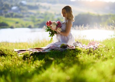 Ormanda genç ve güzel bir kadın gün batımında çimlerin üzerinde piknik yapıyor.