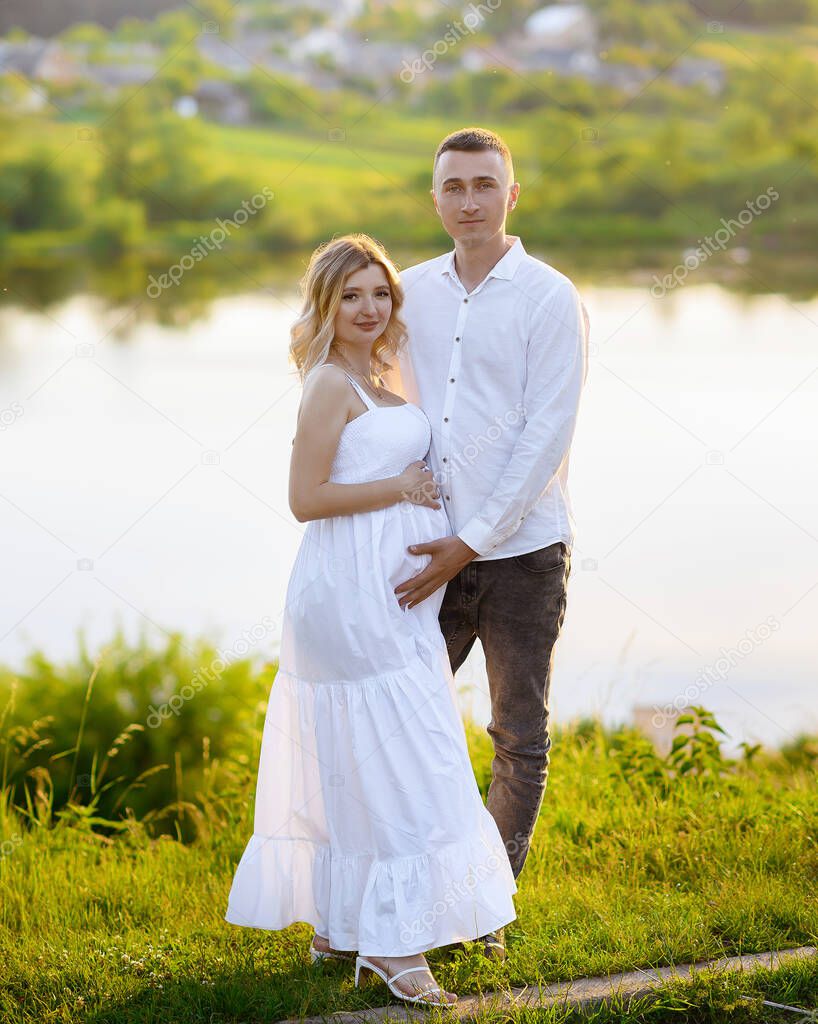 Beautiful young pregnant woman with her husband in the forest at sunset on the background of the lake