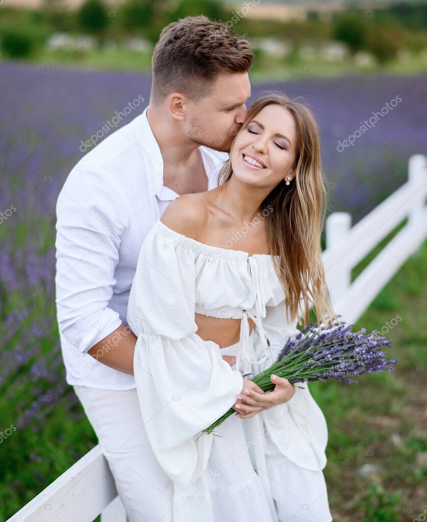 Portrait of a beautiful young couple in light summer clothes in a lavender field at sunset