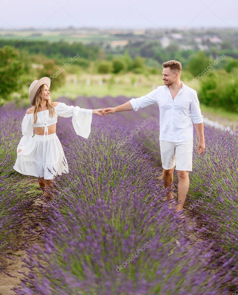 Portrait of a beautiful young couple in light summer clothes hugging in a lavender field at sunset
