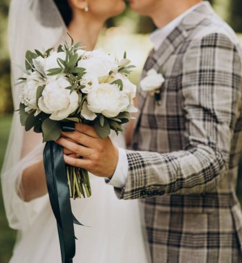 Gelin ve damat ellerinde bir buket beyaz şakayık ve yeşil okaliptüs yaprağı tutuyor. Düğün, düğün, tatil.