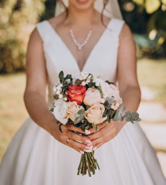Gelinlik giymiş gelin elinde güzel bir buket beyaz, krema, yeşil güller, şakayıklar, güller ve yeşil okaliptüs yaprakları tutuyor..