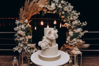 Beyaz üçüncü sınıf düğün pastası. Vanilyalı kek, krem peynirli krema. Pasta pembe ve kırmızı güller ve yeşil yapraklarla süslenmiştir. Düğün pastası.. 