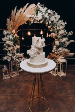 Beyaz üçüncü sınıf düğün pastası. Vanilyalı kek, krem peynirli krema. Pasta pembe ve kırmızı güller ve yeşil yapraklarla süslenmiştir. Düğün pastası.. 