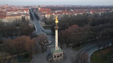 Amazing fly by Angel of Peace in Munich, Germany with the view on the city center, Frauenkirche and Marienplatz on a golden sunrise. Aerial golden hour Friedensengel.