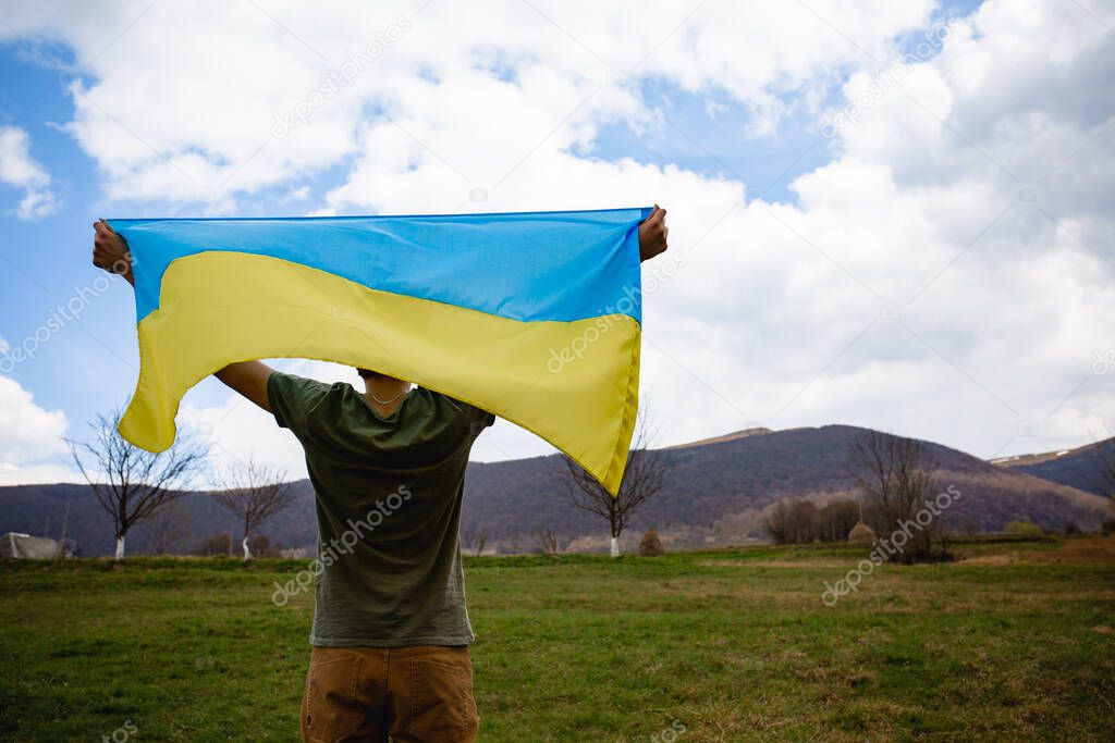 A man holds the Ukrainian flag over his head. On the background of mountains.