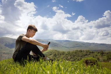 Adam dağın tepesinde oturuyor ve akıllı bir telefona bir mesaj yazıp duruyor. Cep telefonu bağlantısı iyi. Dağ manzarası