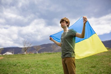 Bir adam Ukrayna bayrağını tutuyor. Savaşı durdurun. Dağların arkasında..