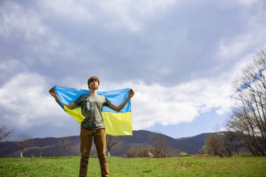 Bir adam Ukrayna bayrağını tutuyor. Savaşı durdurun. Dağların arkasında..