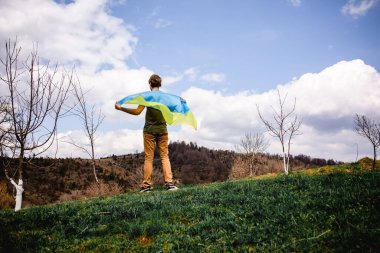 Bir adam Ukrayna bayrağını tutuyor. Savaşı durdurun. Dağların arkasında..