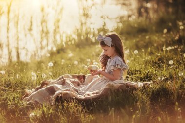 A girl in vintage clothes holds a little chicken in her hands.
