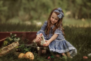 Antika elbiseli bir kız elinde bir kaz tutuyor. Yeşil çimenli arkaplan.