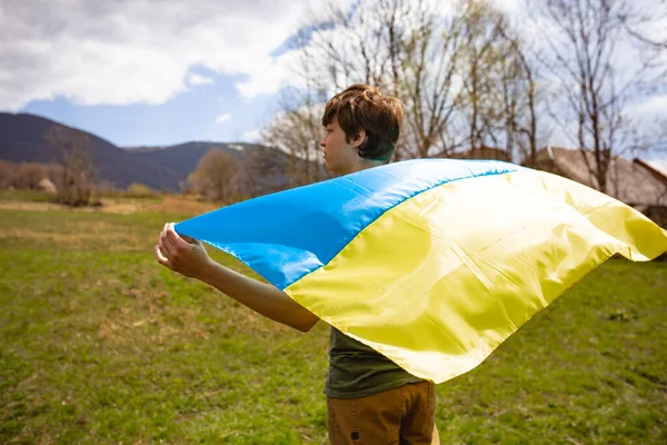 Bir adam Ukrayna bayrağını tutuyor. Savaşı durdurun. Dağların arkasında..
