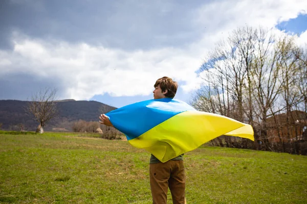 A man holds the Ukrainian flag . Stop war. Against the backdrop of mountains. — Stockfoto