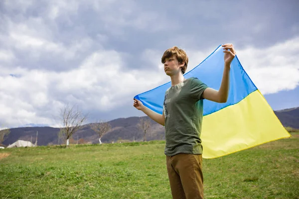 Bir adam Ukrayna bayrağını tutuyor. Savaşı durdurun. Dağların arkasında..