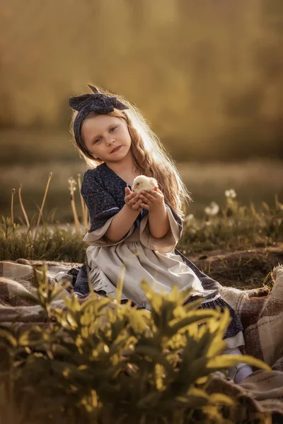 Klasik elbiseli bir kız elinde küçük bir tavuk tutuyor..