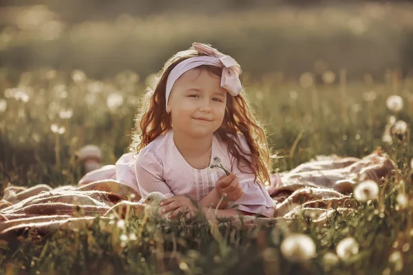 Pembe elbiseli bir kız karahindiba tutuyor. Yaz.