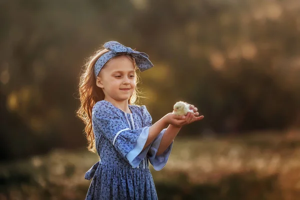 A girl in vintage clothes holds a little chicken in her hands.