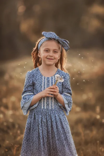 Mavili bir kız elinde bir karahindiba tutuyor. Yaz.