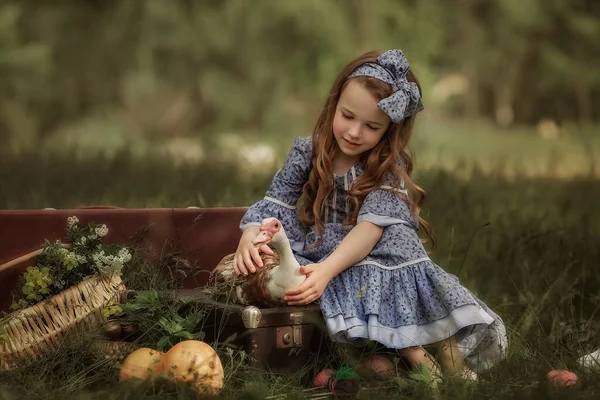 Antika elbiseli bir kız elinde bir kaz tutuyor. Yeşil çimenli arkaplan.