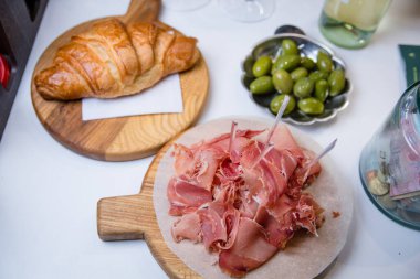 Tahtada dilimlenmiş jamon, hamur işi kruvasan ve yeşil zeytin.