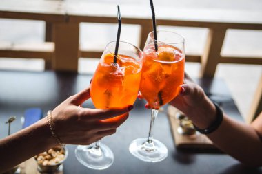 Aperol. İki bardak aperol. İnsanlar aperol bardakları tutuyor..