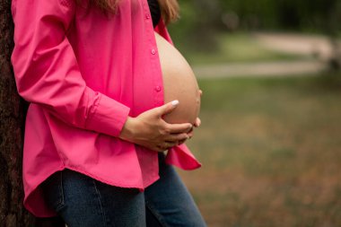 Doğanın bulanık arka planında çıplak karnına dokunan hamile bir kadın. Yüksek kalite fotoğraf