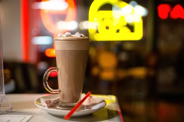 A cup of hot cocoa drink in clear glass with white marshmallows on a blurred cafe background. Milk drink. High quality photo
