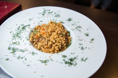 Bir restoranda kuskus. Dereotlu beyaz tabakta kuskus..
