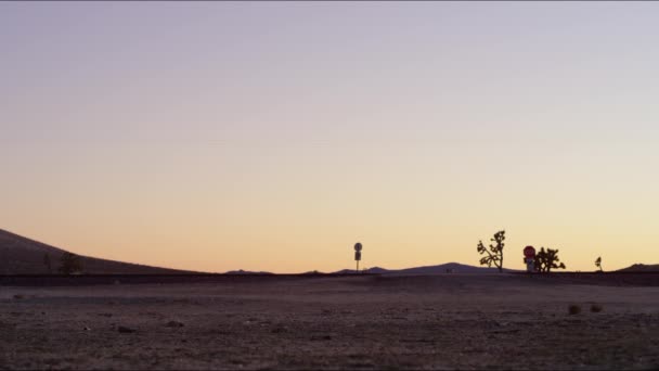 侧向静态框架列车在落日的余晖中高速穿越沙漠景观 岩石般的地形 夕阳西下 一列明亮的火车从前方经过 可以看到一个停车标志 — 图库视频影像