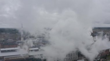 Bulutlu bir günde fabrika bacasından çıkan dumanların arasından uçmak. Bir fabrikada üretilen çevresel kirliliğin 4k hava görüntüsü. Kasabadaki fabrikaların manzarası, havayı kirletiyor.