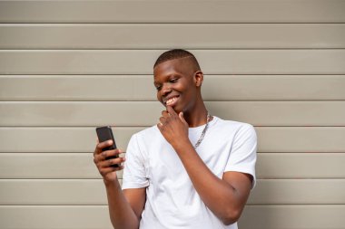 Duvara karşı cep telefonu kullanan Afro genç adam.