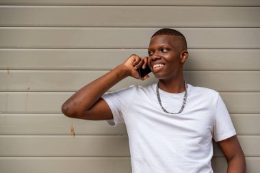 Duvara karşı cep telefonu kullanan Afro genç adam.