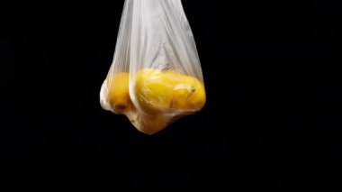 Şeffaf plastik torba içinde olgun sarı limonlar. Kadının eli siyah arkaplanda paketi tutuyor