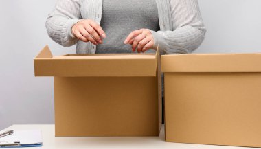 Gri elbiseli kadın beyaz arka planda açık kahverengi kutuyu tutuyor, hareket ediyor, mal gönderiyor ve teslim ediyor.