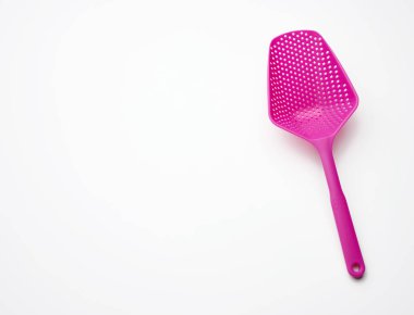 Beyaz arka planda salatayı karıştırmak için delikli pembe plastik kaşık.