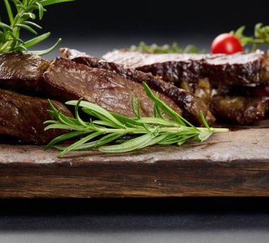 Kahverengi ahşap bir tahtada kızarmış sığır eti dilimlerinin arka planında yeşil biberiye dalı