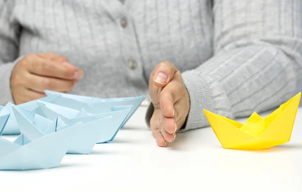 paper boats between a female hand on a white table. Conflict solution concept, negotiator between groups. Searching of decisions