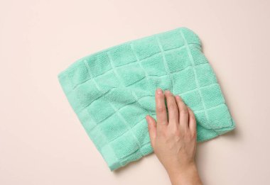 Kadın eli bej arka planda yeşil Terry tekstil havlusunu tutuyor.