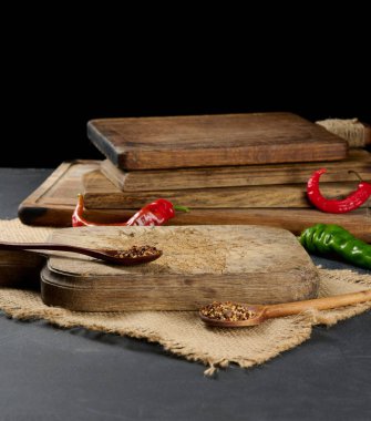 boş mutfak kahverengi ahşap tahta kesme tahtası siyah masanın üzerinde, baharatlı kaşıkların yanında ve taze kırmızı biber, siyah arka plan