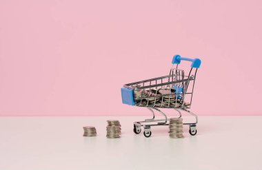 Minyatür metal alışveriş arabası ve beyaz bir masanın üzerinde bir yığın bozuk para. İndirim ve satış kavramı, bütçe tasarrufu. Çevrimiçi ticaret