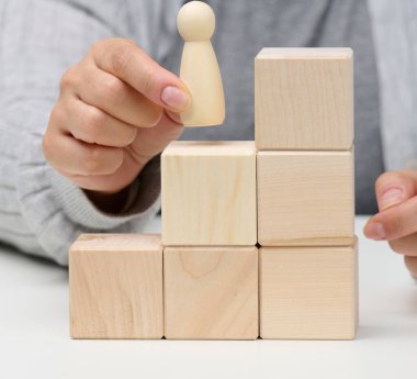 Masanın üzerindeki tahta küplerden ve erkek heykelciklerinden piramitler. Hedeflere ulaşma, kariyer basamaklarını tırmanma kavramı. Tek fikirli kişiliğin tespiti