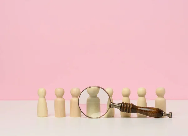 wooden figures of men stand on a pink background and a red plastic magnifying glass. Recruitment concept, search for talented and capable employees, career growth