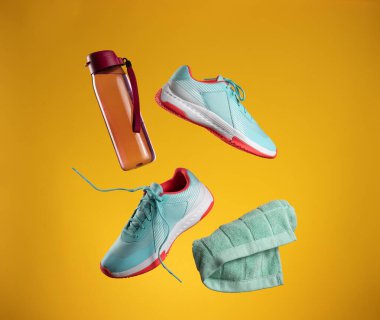 Pembe plastik su şişesi, yeşil havlu ve sarı arka planda yükselen bağcıklı bir çift tekstil mavisi spor ayakkabı. Spor ayakkabıları, koşu.