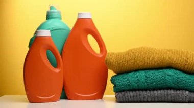 Yıkanmış çamaşır yığını ve sarı arka planda, üzerinde sıvı deterjan bulunan plastik turuncu büyük şişeler. Rutin ev ödevi