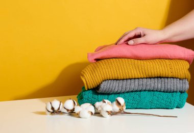 Sarı arka planda örülmüş süveter yığını tutan bir kadın. Çamaşır yıkıyorum, temizlik yapıyorum.