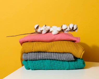 Sarı arka planda katlanmış süveter yığını. Rahat kıyafetler, yıkanmak.