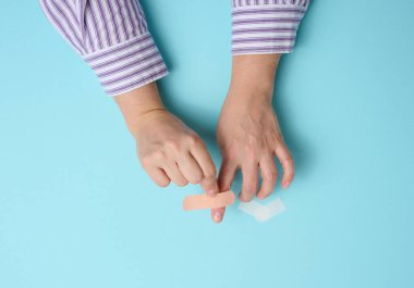 Kadın eli ve kahverengi tıbbi yapıştırıcı cilt yaralanmaları ve kesiklerin tedavisi için, mavi arka plan