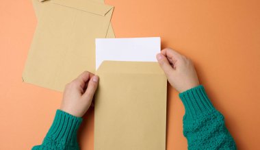 Kadın eli, turuncu arka planda kağıt zarflar tutuyor. Yazışmalar