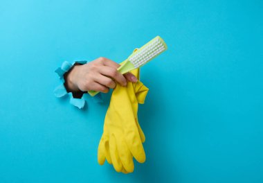 Kadın eli lastik eldiven ve plastik temizleme fırçası tutuyor. Vücudun bir kısmı yırtık bir delikten dışarı fırlıyor.